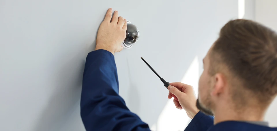 Technicien en uniforme bleu installe une caméra de surveillance extérieure sur façade résidentielle